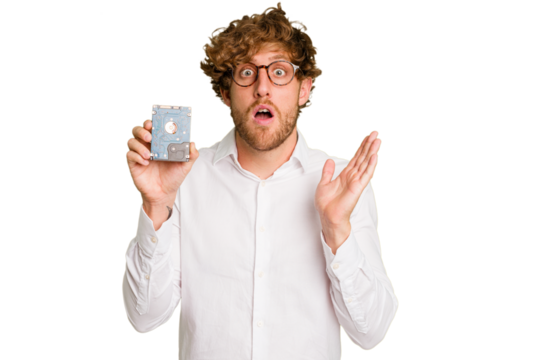 Young caucasian informatic man holding a hard drive isolated on white background surprised and shocked.