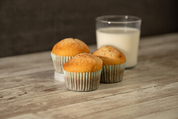 Glass of milk with three freshly baked muffins in the foreground - breakfast, snack, pastries concept