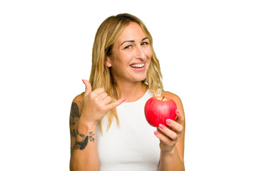 Young caucasian woman holding an apple isolated on green chroma background showing a mobile phone call gesture with fingers.