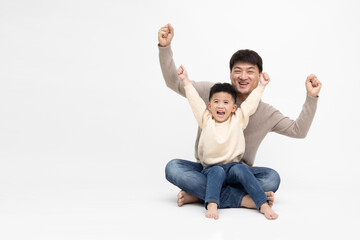 Asian father and son sitting on floor and hands up raised arms from happiness isolated on white...
