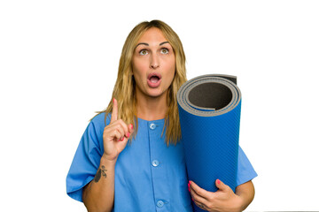 Young caucasian physiotherapist woman holding a mat isolated on green chroma background pointing upside with opened mouth.