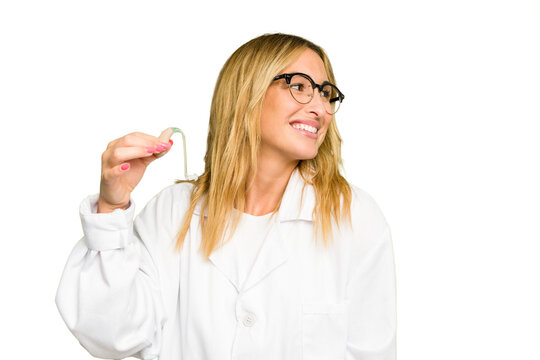 Young otorhinolaryngologist caucasian woman holding hearing aid isolated on green chroma background looks aside smiling, cheerful and pleasant.