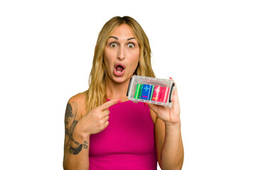 Young caucasian woman holding battery box isolated on green chroma background pointing to the side