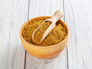 Curry powder in wooden bowl on white wooden background