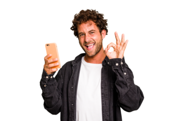 Young caucasian man using mobile phone isolated cheerful and confident showing ok gesture.
