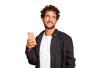 Young caucasian man using mobile phone isolated looks aside smiling, cheerful and pleasant.