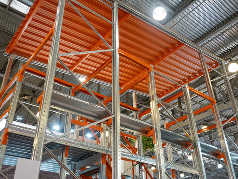 Warehouse rack. Furniture for long-term storage of goods. Steel warehouse structure for storing boxes. Grey-orange shelves inside warehouse. Mezzanine shelving. Furniture for storage logistics