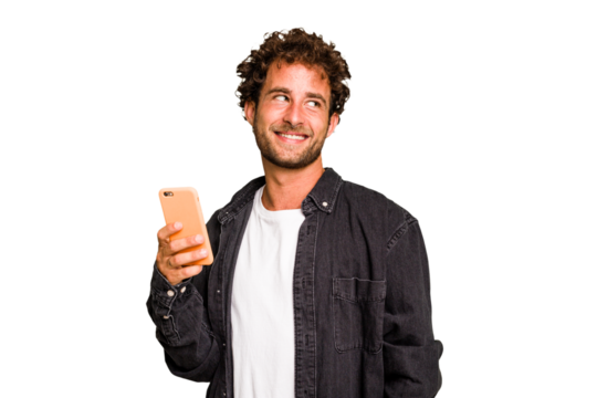 Young caucasian man using mobile phone isolated looks aside smiling, cheerful and pleasant.