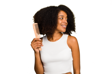 Young african american woman holding hair comb isolated looks aside smiling, cheerful and pleasant.