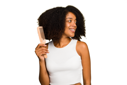 Young african american woman holding hair comb isolated looks aside smiling, cheerful and pleasant.
