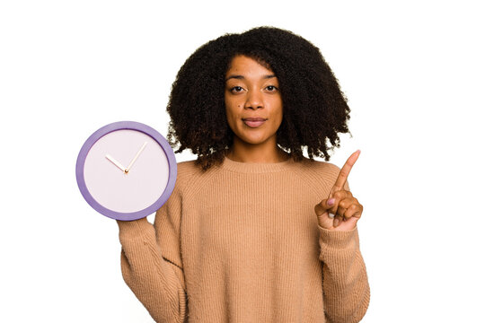Young African American holding a clock isolated showing number one with finger.