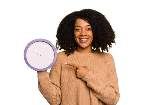 Young African American holding a clock isolated smiling and pointing aside, showing something at blank space.