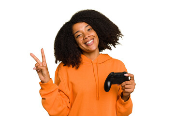 Young African American woman holding a game controller isolated joyful and carefree showing a peace symbol with fingers. © Asier