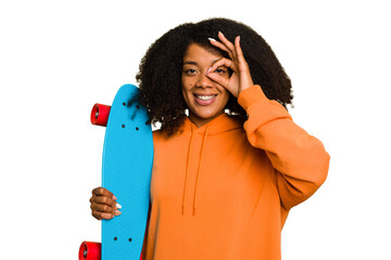 Young skater African American woman holding a little skate isolated excited keeping ok gesture on eye. © Asier
