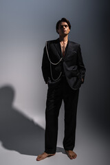 Obraz premium full length of barefoot man in trendy suit with pearls posing with hands in pockets on dark grey