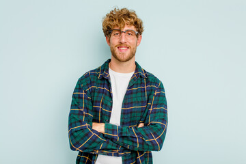 Young caucasian man isolated on blue background who feels confident, crossing arms with determination.