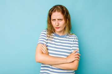 Young caucasian woman isolated on blue background frowning face in displeasure, keeps arms folded.