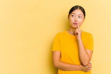 Young Asian woman isolated on yellow background looking sideways with doubtful and skeptical expression.