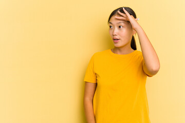 Young Asian woman isolated on yellow background looking far away keeping hand on forehead.