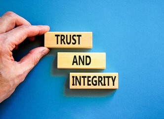 Trust and integrity symbol. Concept words Trust and integrity on wooden blocks. Businessman hand. Beautiful blue background. Business, psychological and trust and integrity concept. Copy space.