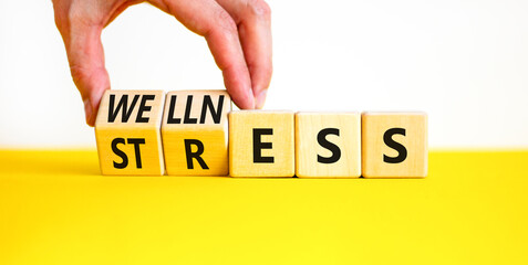 Stress or wellness symbol. Concept words Stress or Wellness on wooden cubes. Businessman hand. Beautiful yellow table white background. Business stress or wellness concept. Copy space.
