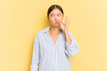 Young Asian woman isolated on yellow background with fingers on lips keeping a secret.