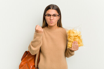 Young student Indian woman holding crips isolated on white background showing fist to camera, aggressive facial expression.