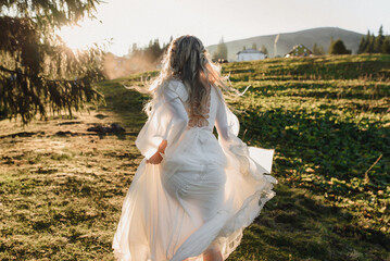 Bride in wedding dress runs at sunset in the mountains