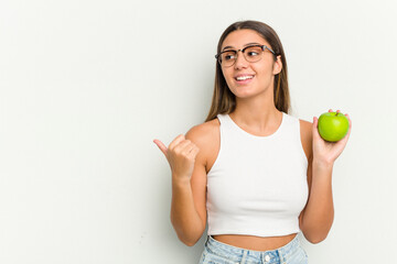 Young Indian woman holding an apple isolated on white background points with thumb finger away, laughing and carefree.