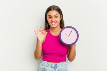 Young Indian woman holding a clock isolated on white background cheerful and confident showing ok gesture.