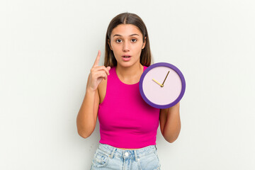 Young Indian woman holding a clock isolated on white background having an idea, inspiration concept.