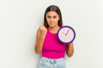 Young Indian woman holding a clock isolated on white background showing fist to camera, aggressive facial expression.