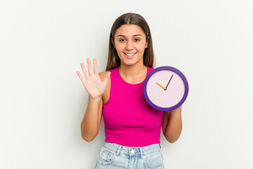 Young Indian woman holding a clock isolated on white background smiling cheerful showing number...