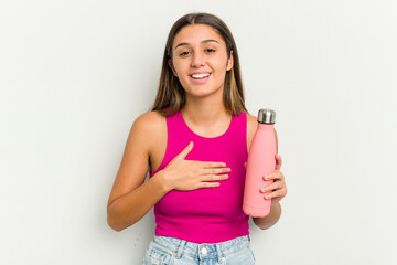 Young indian woman holding a pink thermo isolated on white background laughs out loudly keeping hand on chest.