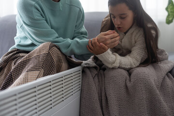 At the electric heater, people are warming themselves, covered with a warm blanket at home. hands...