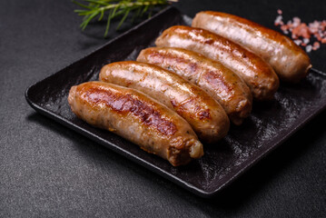 Tasty grilled sausages with spices and herbs on a black slate plate