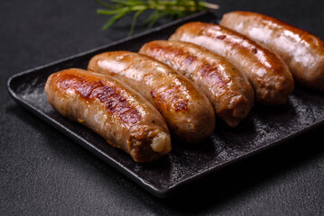 Tasty grilled sausages with spices and herbs on a black slate plate
