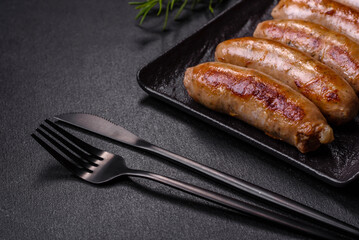 Tasty grilled sausages with spices and herbs on a black slate plate