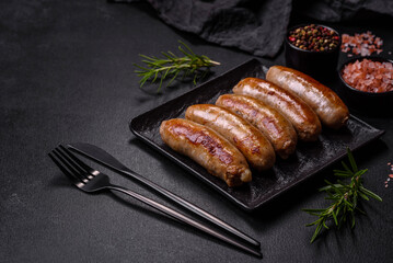 Tasty grilled sausages with spices and herbs on a black slate plate