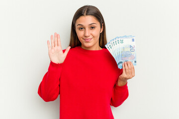 Young Indian woman holding a banknotes isolated on white background smiling cheerful showing number five with fingers.