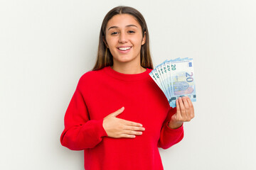 Young Indian woman holding a banknotes isolated on white background laughs out loudly keeping hand on chest.