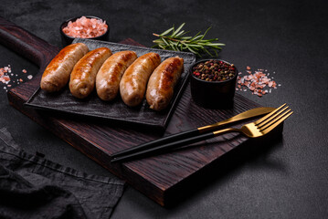 Tasty grilled sausages with spices and herbs on a black slate plate