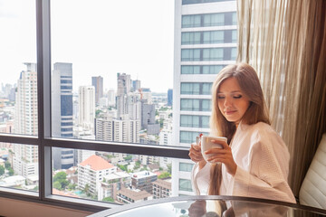 Fototapeta premium Woman in bathrobe with coffee cup sitting in modern hotel or apartment