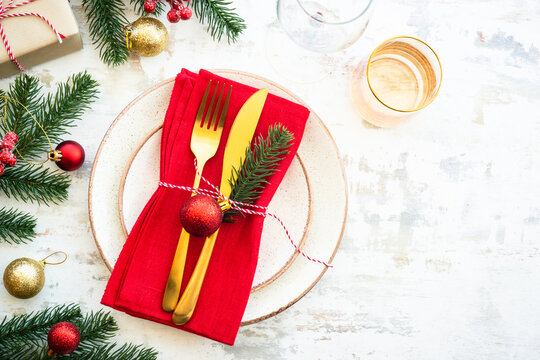 Christmas table setting with craft plate, golden cutlery and christmas decorations on white wooden background. Flat lay image with copy space.