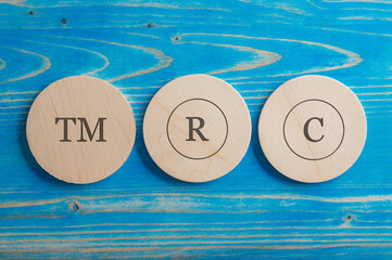 TM, R and C signs each written on its own wooden cut circle
