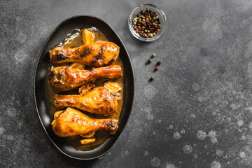 Spicy roasted chicken legs in cast iron skillet on dark background. Top view, copy space.