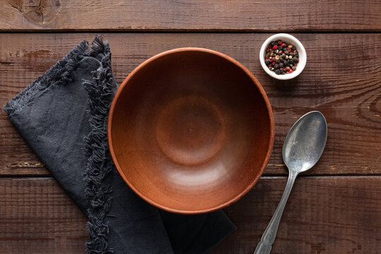 Empty terracotta ceramic bowl, spoon, spices and table linen textile. Table setting with copy space for text or design elements, top view