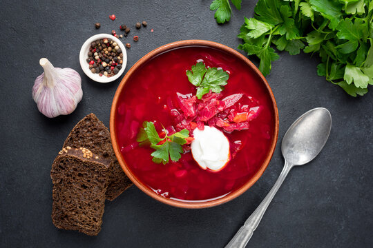 Beet borscht with sour cream, garlic and rye bread on black stone background. Top view. Ukrainian culture food