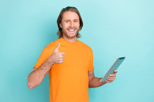 Photo of confident cool man wear orange t-shirt reading modern device thumb up isolated turquoise color background