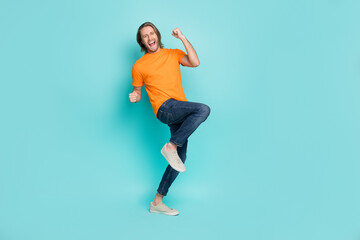 Fototapeta na wymiar Full length photo of charming lucky guy dressed orange t-shirt smiling rising fists isolated teal color background